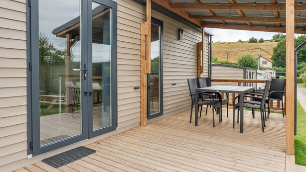 Una terraza con mesa y sillas, una puerta corrediza de vidrio y una estructura de pérgola.