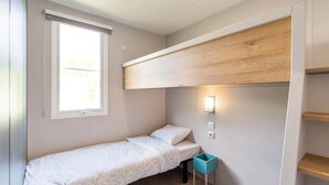 A small, single-bed room with a window, a wall-mounted light, and a wooden shelf. - Camping Papillon Bouillon - Family Vacation Home 6 (Bouillon)