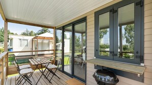 A covered outdoor patio with a barbecue grill, wooden tables, and chairs. - Camping Papillon Bouillon - Premium Quiet (Bouillon)