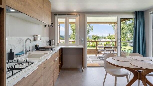 A modern kitchen with wooden cabinets, a gas stove, and a view to an outdoor dining area. - Camping Papillon Bouillon - Premium Quiet (Bouillon)
