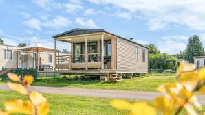 A mobile home with a covered porch and a fenced yard. - Camping Papillon Bouillon - Premium Quiet (Bouillon)