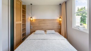 Een slaapkamer met een houten hoofdbord, twee bedlampen, een bed met een decoratieve spreidek en uitzicht op het landschap door een raam.