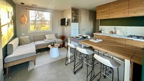 A modern kitchen with a wooden countertop, bar stools, and a built-in stove. - Camping Papillon Kinrooi - 88 (Kinrooi)