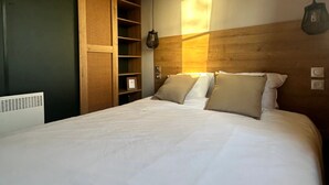 A neatly made bed with a wooden headboard, a small shelf unit, and a pendant light. - Camping Papillon Kinrooi - 88 (Kinrooi)