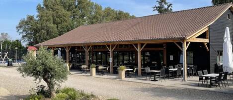Een terras met tafels en stoelen, een tafeltennistafel en een overdekte paviljoe met pannendak.