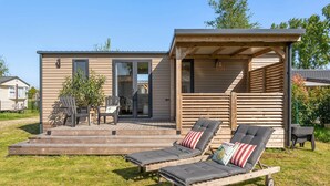 A wooden cabin with a deck, two lounge chairs, and a covered patio area. - Camping Papillon Kinrooi - La Casetta (Kinrooi)