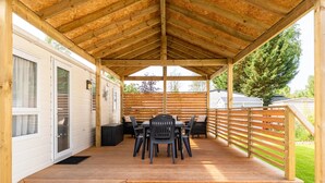 Une terrasse extérieure couverte, dotée d’une plateforme en bois, d’une table avec des chaises et d’une clôture en bois.