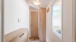 Un couloir étroit avec une porte en bois, une fenêtre en verre dépoli et un luminaire au plafond.