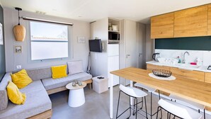 Un espace de vie compact comprenant un canapé, une table basse et un coin cuisine doté d’un plan de travail en bois et de tabourets de bar.