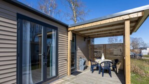 Une maison moderne dotée d’une terrasse en bois, d’une porte-fenêtre coulissante et d’un patio couvert aménagé avec du mobilier d’extérieur.
