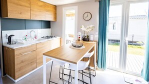 Une cuisine moderne avec des meubles en bois, un plan de travail blanc et un coin repas comprenant une table en bois et des chaises blanches.