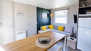 Une cuisine compacte avec une table en bois, un réfrigérateur encastré et un canapé avec des coussins jaunes.