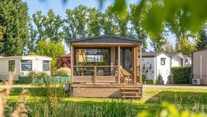 A wooden cabin with a deck, surrounded by a pond and greenery.
