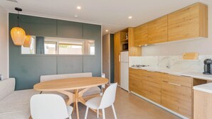 A modern kitchen with wooden cabinets, a white countertop, and a dining area with a wooden table and white chairs.