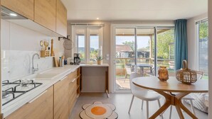 A modern kitchen with wooden cabinets, a gas stove, and a dining area with a round table and chairs. - Camping Papillon Kinrooi - 139 (Kinrooi)
