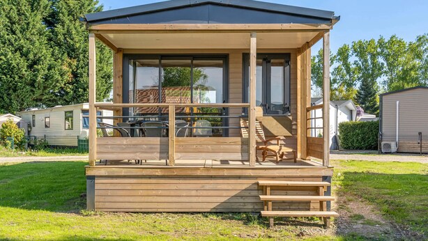 A wooden cabin with a covered porch, large windows, and a staircase leading to an upper level. - Camping Papillon Kinrooi - 139 (Kinrooi)