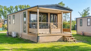 A single-story mobile home with a covered porch, a small deck, and a patio area. - Camping Papillon Kinrooi - 139 (Kinrooi)