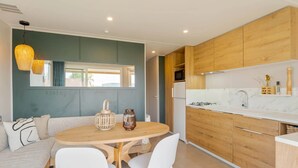 A modern kitchen with wooden cabinets, a white countertop, and a dining area with a round table and chairs. - Camping Papillon Kinrooi - 139 (Kinrooi)