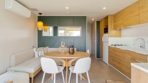 A modern kitchen with wooden cabinets, a round dining table with white chairs, and a built-in oven. - Camping Papillon Kinrooi - 139 (Kinrooi)