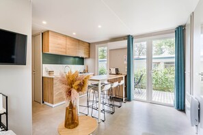 A modern kitchen with wooden cabinets, a dining area with bar stools, and a large sliding glass door leading to an outdoor patio. - Camping Papillon Kinrooi – Family Vacation Home (6P) (Kinrooi)