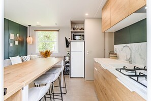 A modern kitchen with a wooden dining table, white chairs, a built-in oven, and a marble countertop with a sink. - Camping Papillon Kinrooi – Family Vacation Home (6P) (Kinrooi)
