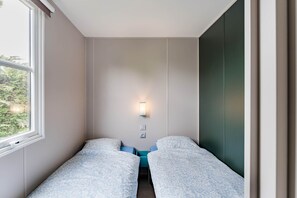 A room with two beds, a window, a wall-mounted light, and a view of greenery outside. - Camping Papillon Kinrooi – Family Vacation Home (6P) (Kinrooi)