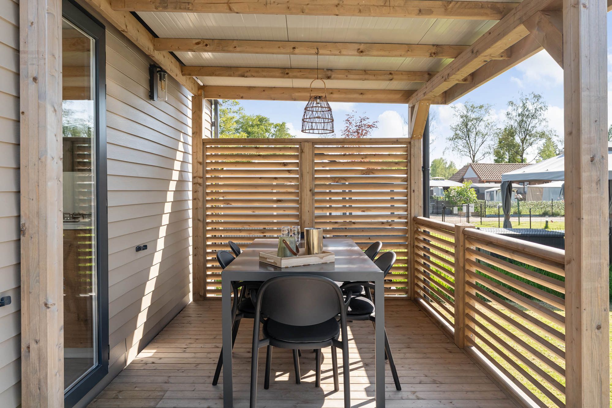 Uma área de estar coberta ao ar livre, com mesa e cadeiras, luminária pendente e vista para os arredores.