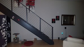 Eine Treppe mit schwarzer Geländer, eine Katzenliege, ein rotes Kissen und ein gerahmtes Bild an der Wand.
