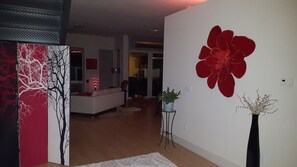Ein modernes Wohnzimmer mit einem großen Gemälde einer roten Blume, einem weißen Sofa und einem kleinen Tisch mit einer Pflanze.