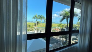 A room with a large window, curtains, and a view of palm trees and a road. - PGA Golf Course 3-bedroom condo AC & VIEWS- steps to the Beach, Clubhouse & Pool (Río Grande)