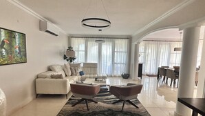 A spacious living room with a white sofa, two armchairs, a coffee table, and a large window with sheer curtains. - PGA Golf Course 3-bedroom condo AC & VIEWS- steps to the Beach, Clubhouse & Pool (Río Grande)