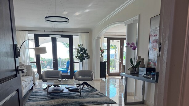 A spacious living area with a large window, a sofa, a coffee table, and a modern chandelier. - PGA Golf Course 3-bedroom condo AC & VIEWS- steps to the Beach, Clubhouse & Pool (Río Grande)