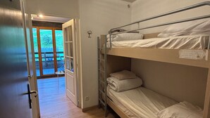 Een slaapzaal met stapelbedden, een houten vloer en een deur naar een balkon.