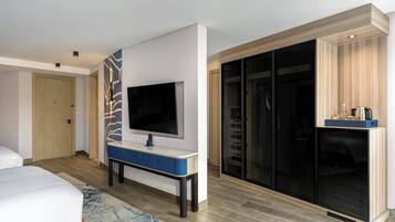 Une chambre d’hôtel moderne équipée d’un lit, d’un téléviseur à écran plat fixé au mur, d’un petit bureau et d’une armoire avec un miroir.