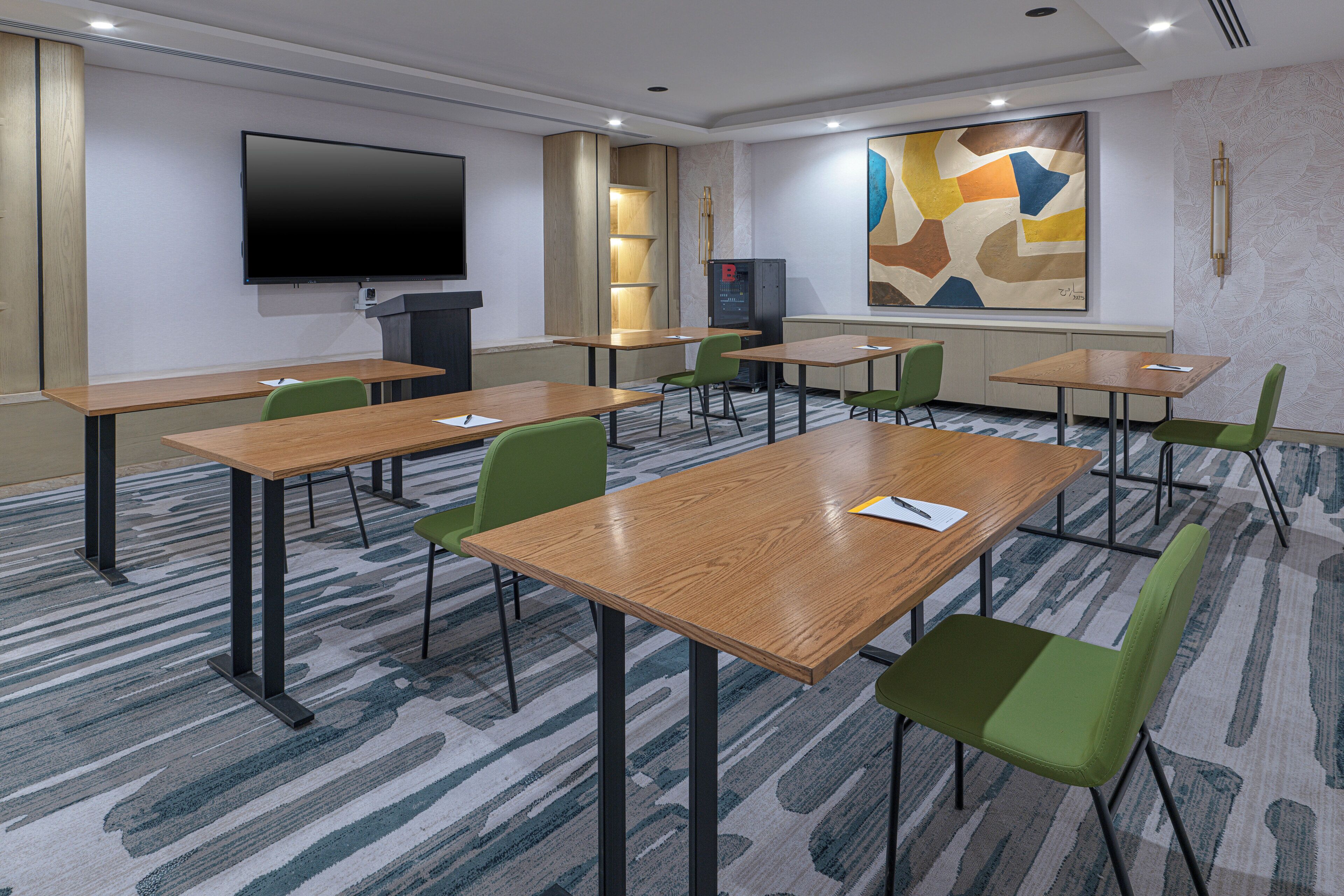 A conference room with multiple tables and chairs, a flat-screen TV, and abstract wall art.