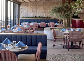 Ein Restaurant mit runden Tischen, gepolsterten Sitzplätzen und einem großen Fenster.