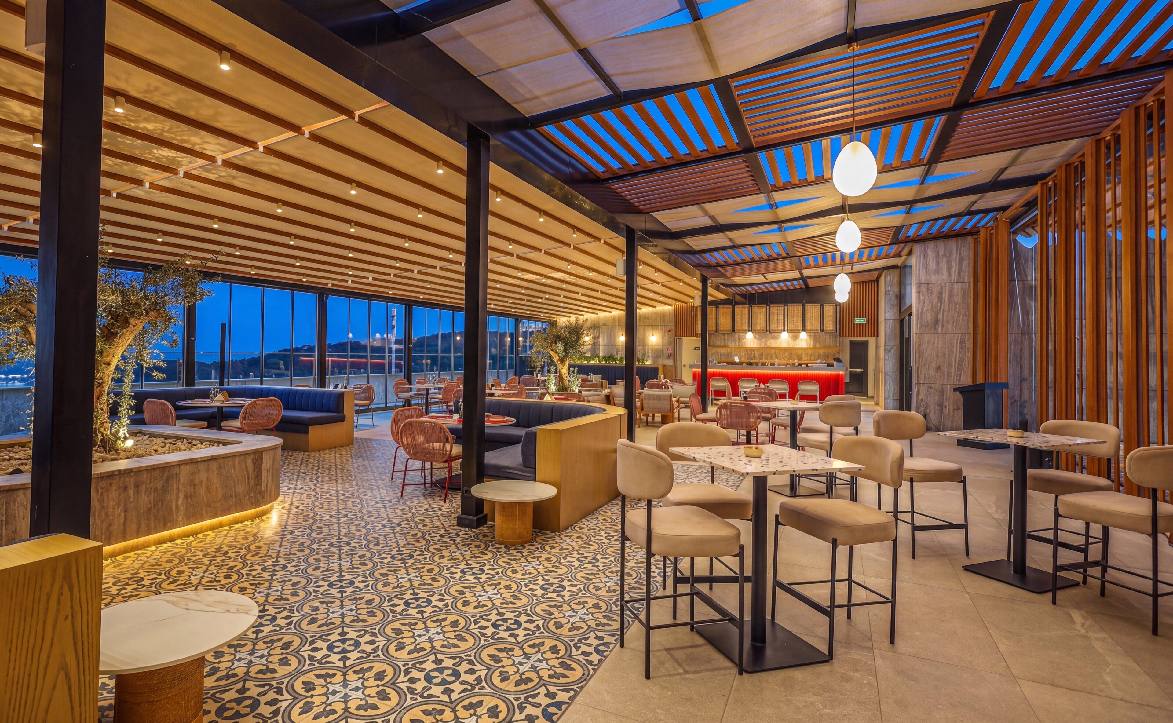 A modern restaurant with a high ceiling, patterned floor, and a bar area.