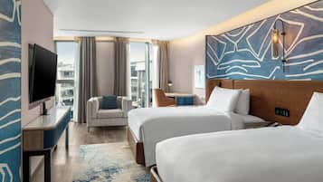 Une chambre d’hôtel avec deux lits, une télévision, un bureau, une chaise, une lampe et une vue sur la ville.