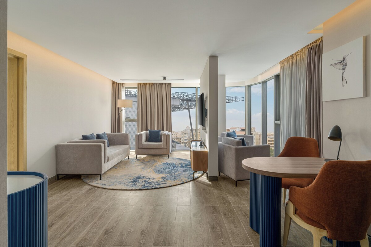 Ein modernes Hotelzimmer mit Wohnbereich, einem Esstisch und Blick auf die Stadt.