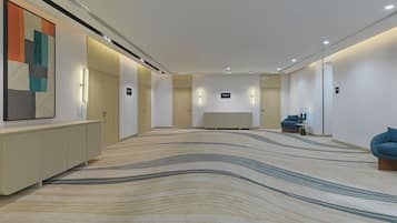 A modern hotel lobby with a patterned carpet, a large abstract painting, and a seating area with a blue chair.
