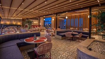 A modern restaurant interior with multiple seating areas, including round tables and sofas, and a patterned floor.