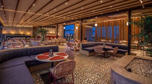 A modern restaurant interior with multiple seating areas, including round tables and sofas, and a patterned floor.