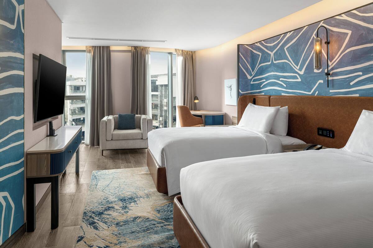 Une chambre d’hôtel avec deux lits, une télévision, un bureau, une chaise, une lampe et une vue sur la ville.