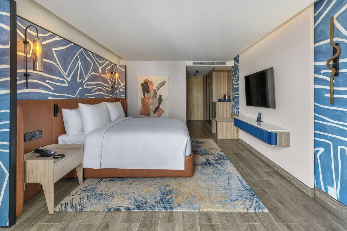 Une chambre d’hôtel moderne avec un grand lit, une table de chevet avec un téléphone, un téléviseur fixé au mur et un tableau accroché au mur.
