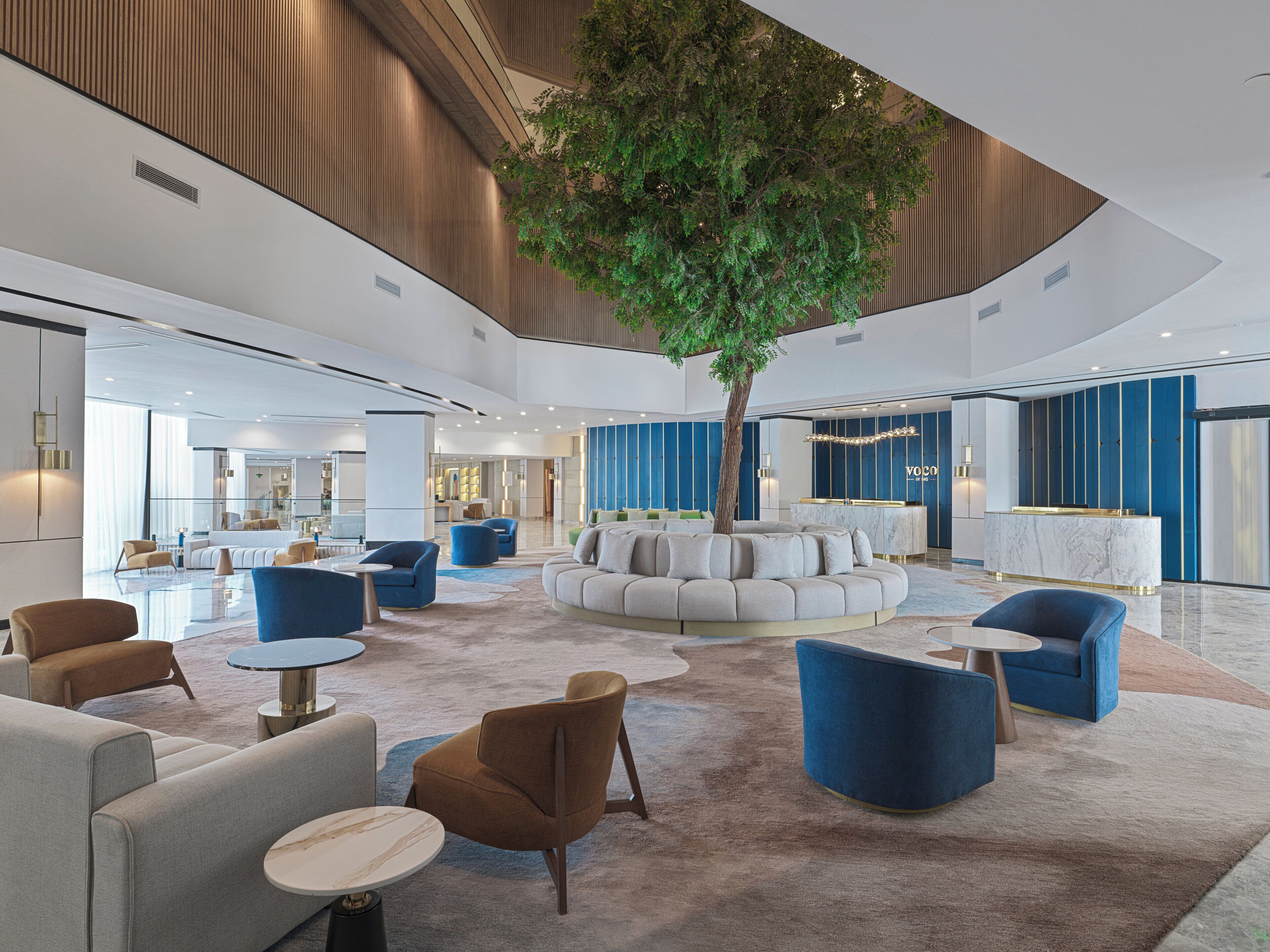 A spacious lobby with a central seating area, a reception desk, and a large tree.