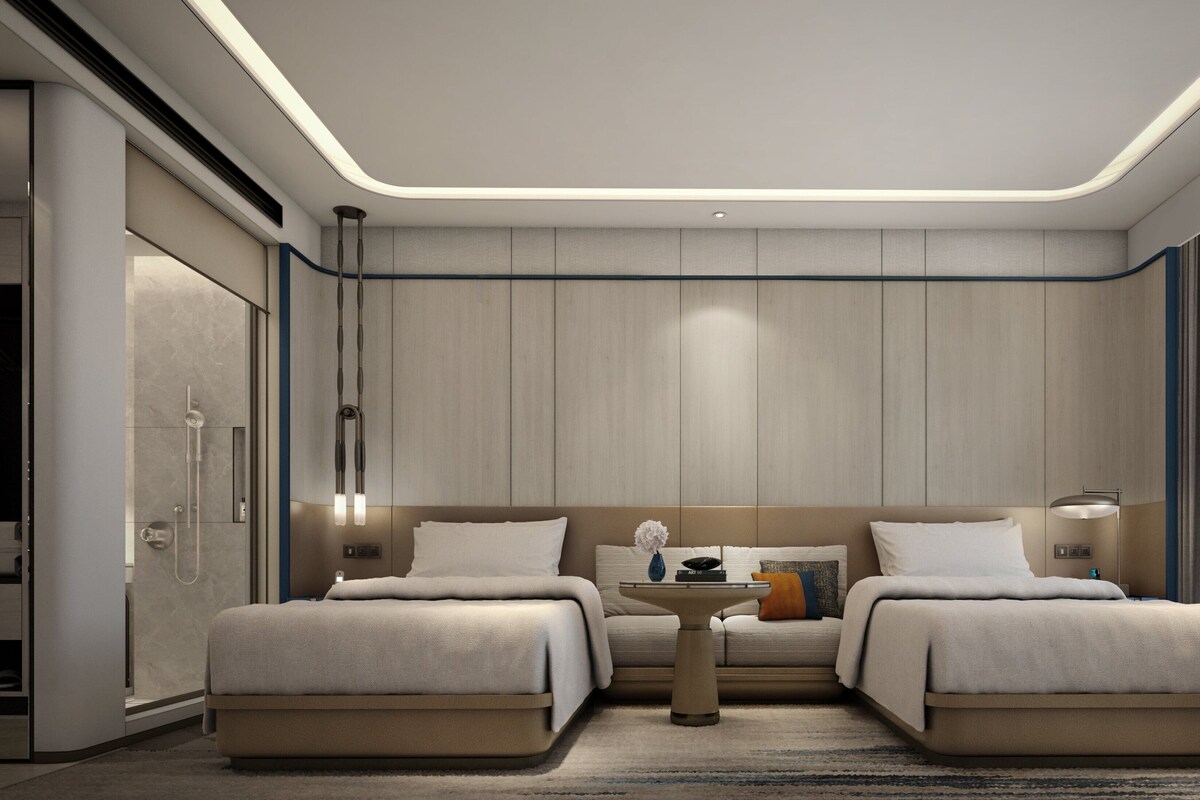 A modern hotel room with two beds, a small table, and a view of the city.