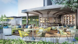 An outdoor seating area with modern furniture, a covered section with bookshelves, and a view of a tall building in the background. - Crowne Plaza Dhaka Airport by IHG (Dhaka)