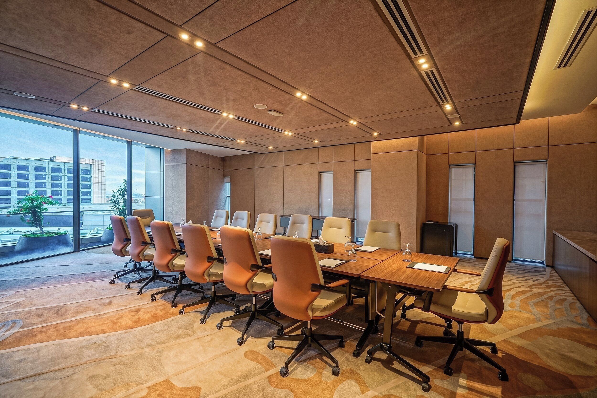 A conference room with a long table, multiple chairs, and a view of the cityscape through large windows.