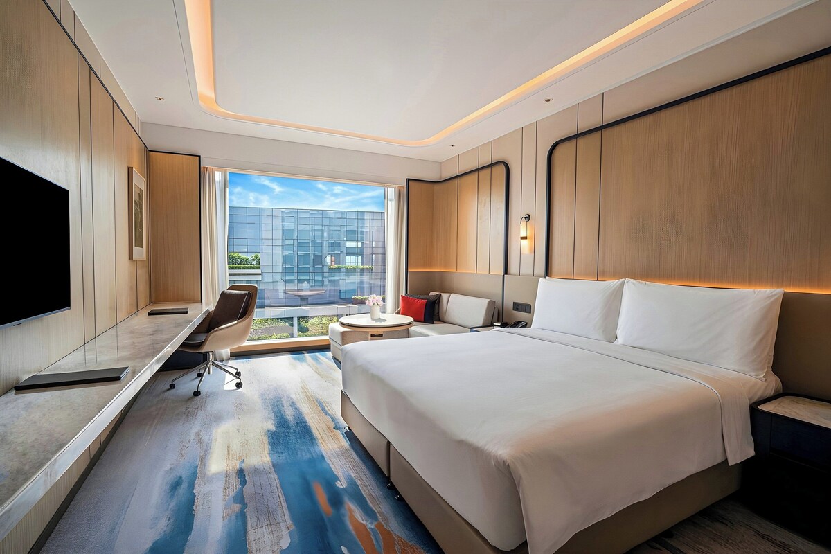 A modern hotel room with a large bed, a desk, a chair, and a TV.