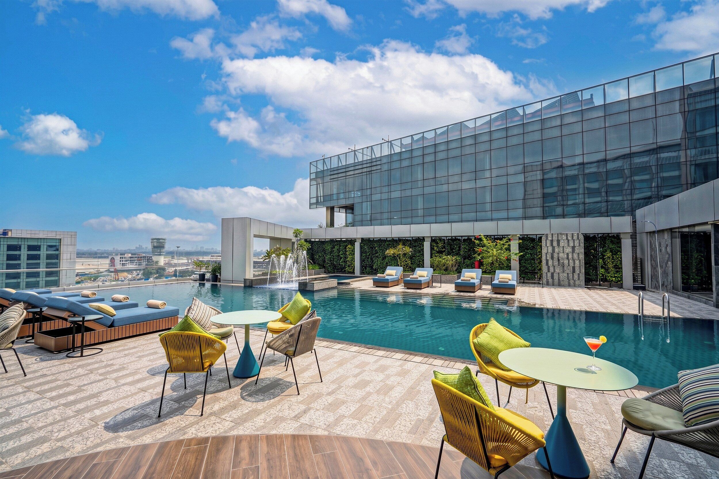 A rooftop pool area with lounge chairs, a small table, and a view of the city skyline.